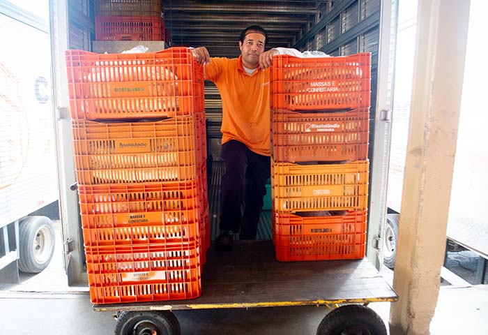 Colaborador da Campodoro com uniforme laranja organizando caixas plásticas identificadas em caminhão, em operação de carga